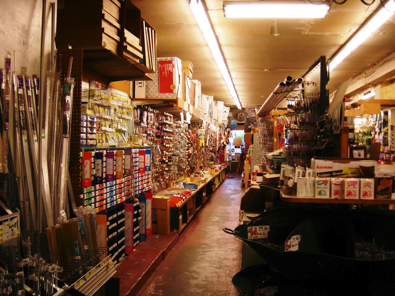 A hardware trade counter: fixings, hand tools and fittings racked floor to ceiling down a narrow aisle.
